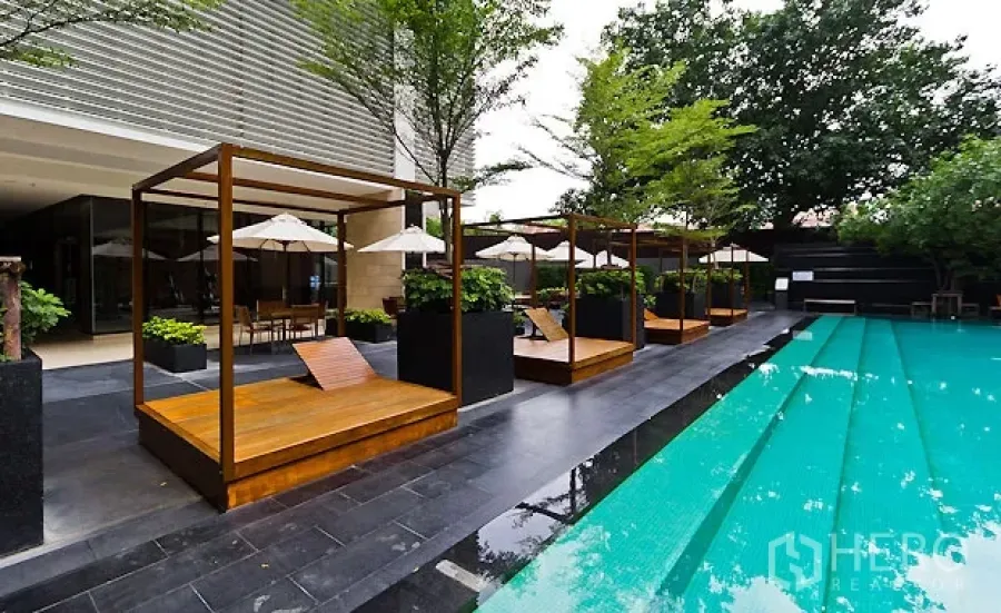 Condominium for rent or sale in Khlong Toei, Bangkok - Resort-style outdoor swimming pool with wooden cabanas and sun loungers at a modern Bangkok condominium.