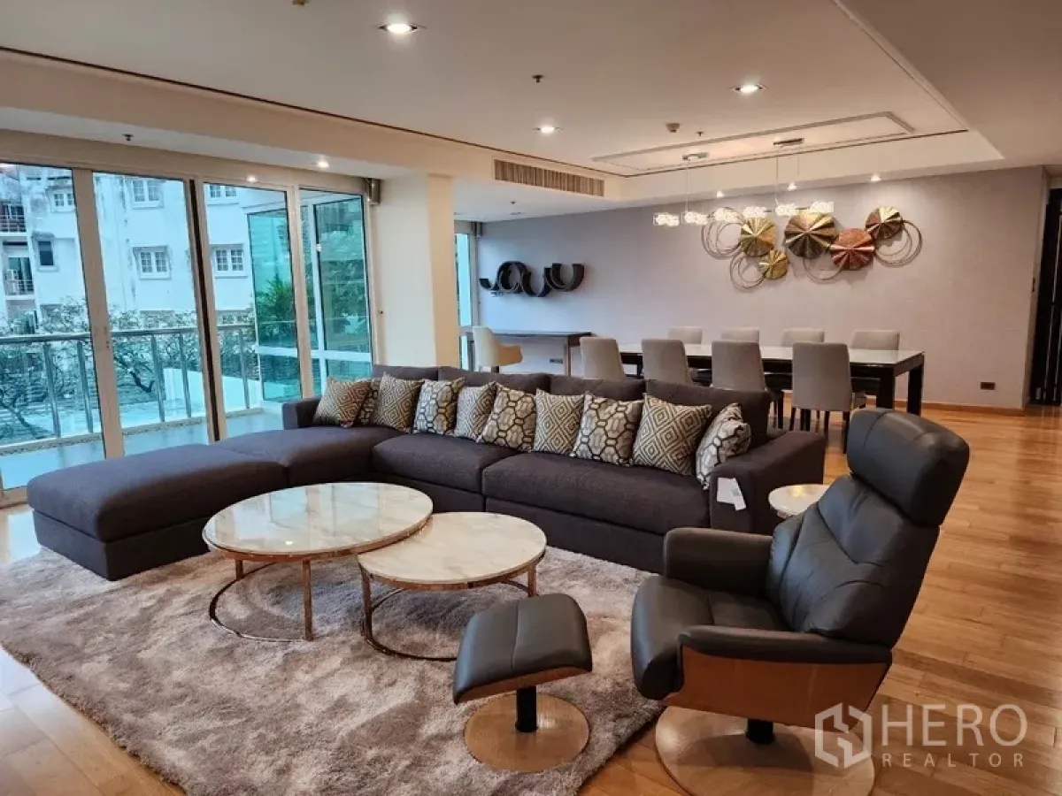 Condominium for rent in Khlong Toei, Bangkok - Spacious living room of luxury Khlong Toei condo with L‑shaped sofa, balcony and wood floors.