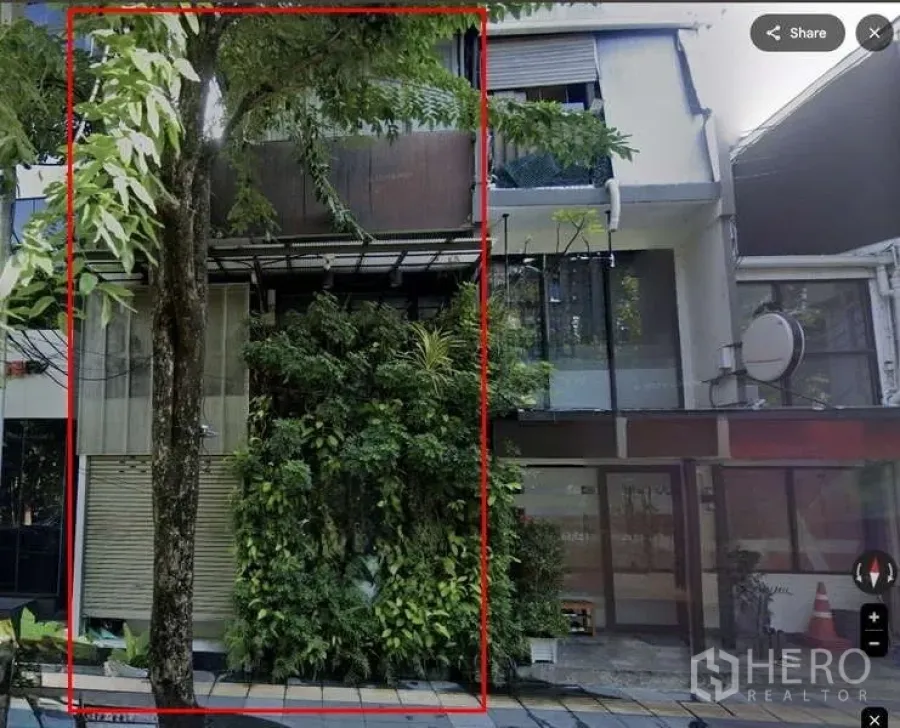 Shophouse for rent in Pathum Wan, Bangkok - Three-storey shophouse facade in Bangkok with a glass storefront, roll-up shutter, and lush vertical garden wall shaded by a street tree.