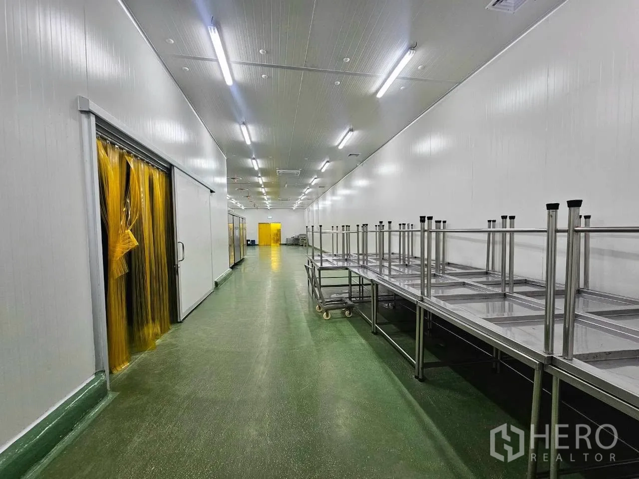 Factory for rent in Mueang Samut Sakhon, Samut Sakhon - Green-floor corridor with stainless worktables and yellow PVC curtains.