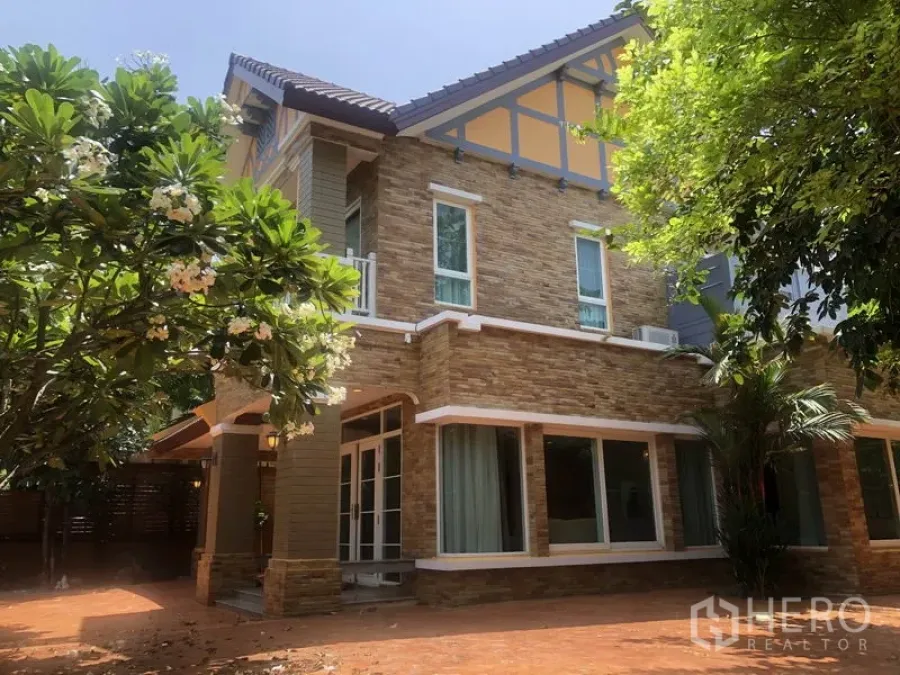 Detached House for rent or sale in Pak Kret, Nonthaburi - Two-storey detached house with stone facade, large windows and shaded garden.
