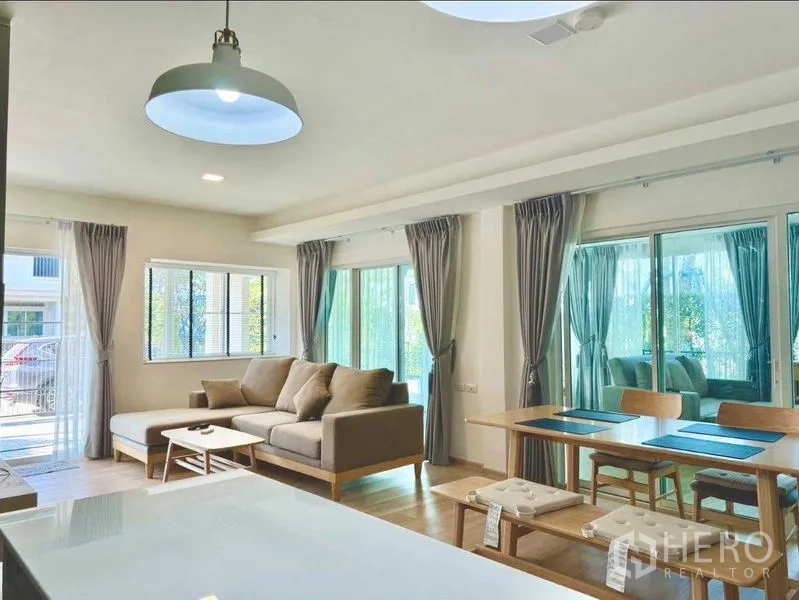 Townhouse for rent or sale in Prawet, Bangkok - Sunlit lounge and dining area wrapped by large windows and sliding doors with gray curtains.