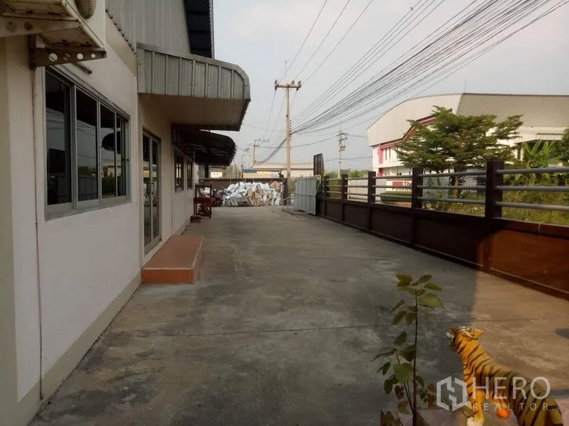 Factory for rent in Lat Lum Kaeo, Pathum Thani - Front driveway by office facade with power poles and nearby buildings.