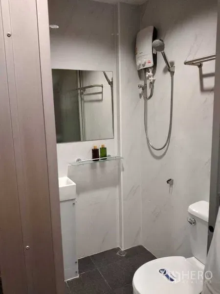 Shophouse for rent in Watthana, Bangkok - Modern bathroom with electric shower, vanity, mirror, and toilet in white tile.