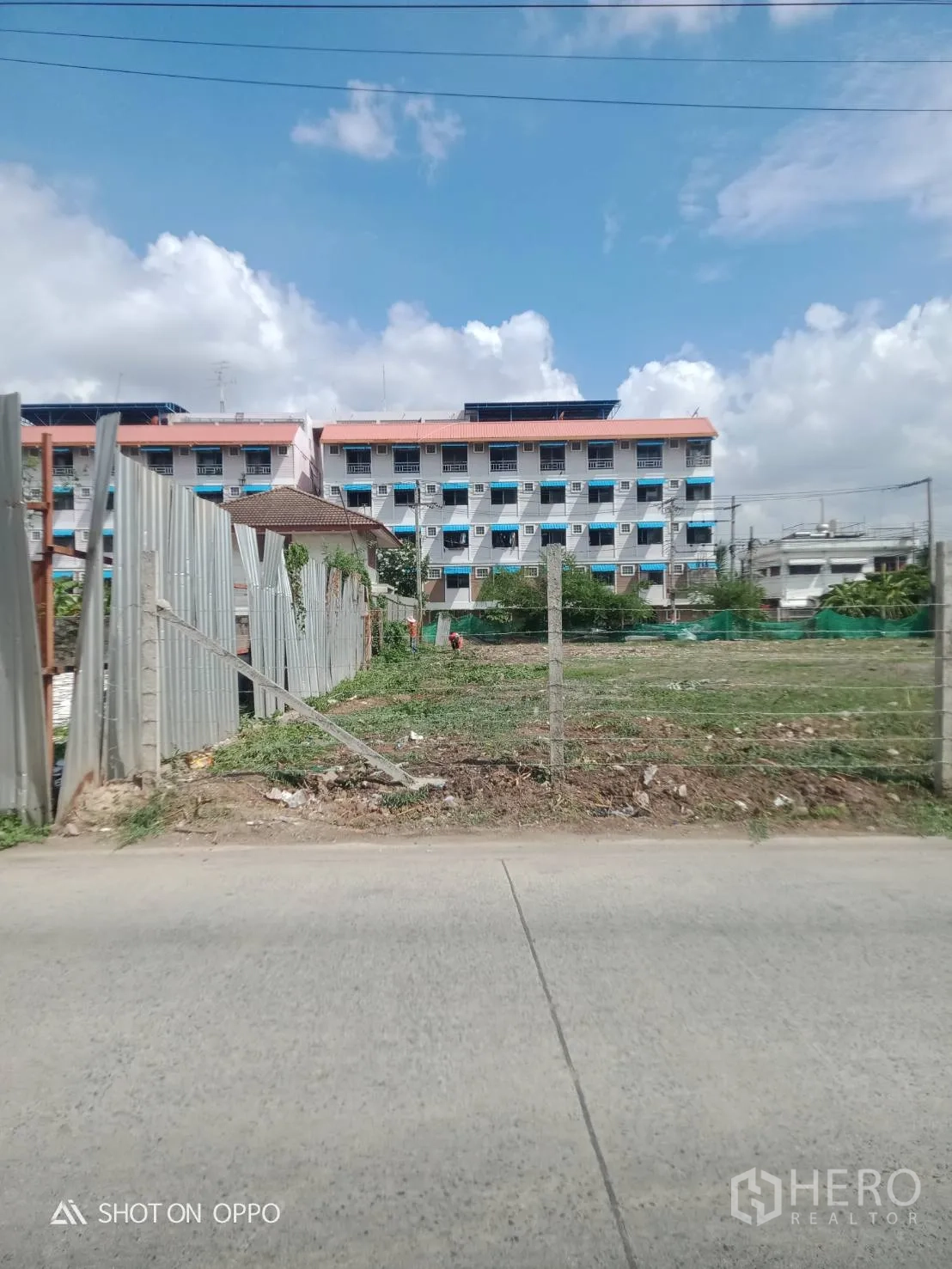 地 出租在Khan Na Yao, Bangkok - 从街道望向围栏开口处的地块，附近有公寓楼。