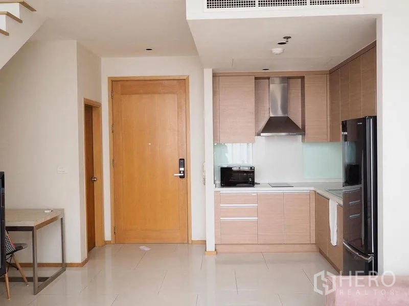 Condominium for rent in Khlong Toei, Bangkok - Light wood L-shaped kitchen with built-in hob, hood and black refrigerator.