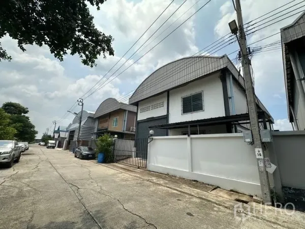 Factory for rent in Bang Bua Thong, Nonthaburi - Street view of a row of modern small factories with parking and overhead power lines in a quiet industrial lane.