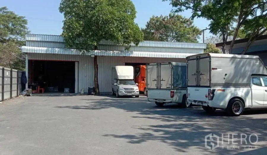 Warehouse for rent in Khlong Sam Wa, Bangkok - Front of warehouse with spacious driveway and parked box trucks, showing ample maneuvering space for logistics.