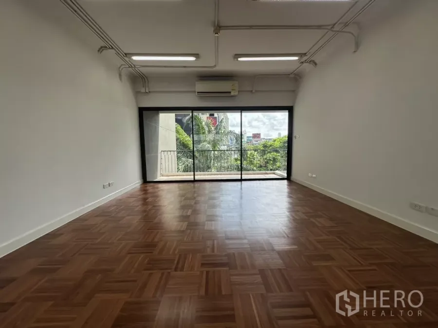 Office Space for rent in Watthana, Bangkok - Open-plan office with parquet flooring, split-type AC and large sliding doors leading to a balcony with city and greenery views.