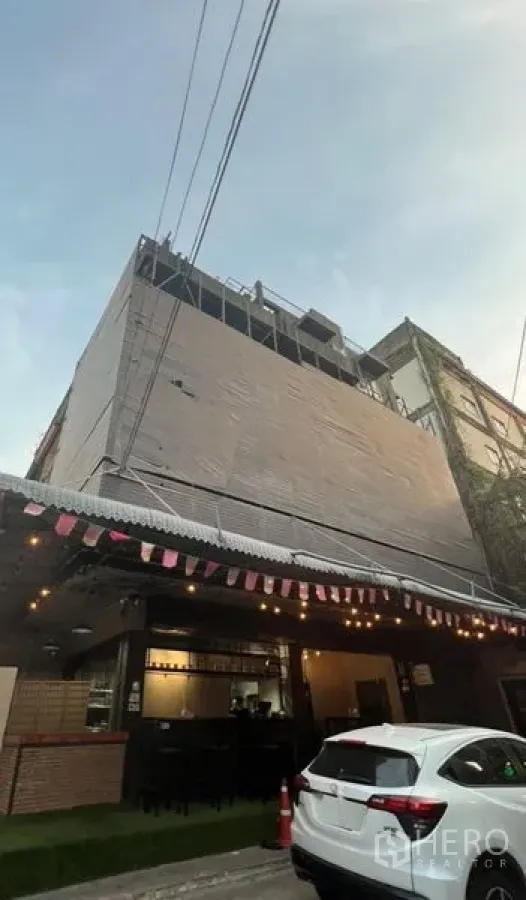 店屋 出租或出售在Watthana, Bangkok - 多层店屋外立面，临街一层为咖啡馆风格门面，带雨棚与夜间灯光。