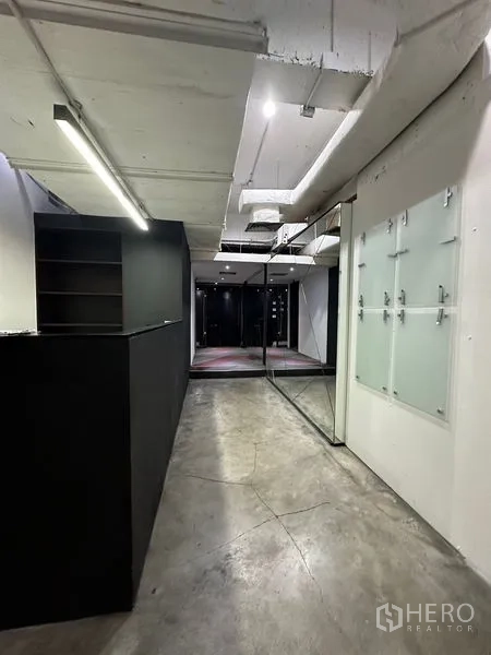 Office Space for rent in Watthana, Bangkok - Reception corridor with black counter, mirrors, glass doors, and concrete flooring.