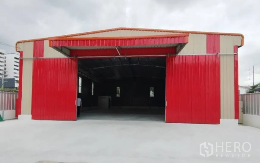 Warehouse for rent in Bang Khen, Bangkok - Front view of metal-clad warehouse with wide red sliding doors and a broad concrete loading apron.