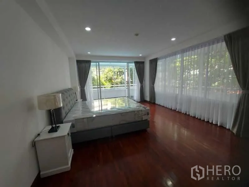 Condominium for rent in Watthana, Bangkok - Corner bedroom with floor-to-ceiling windows and sliding door to a balcony with green views.