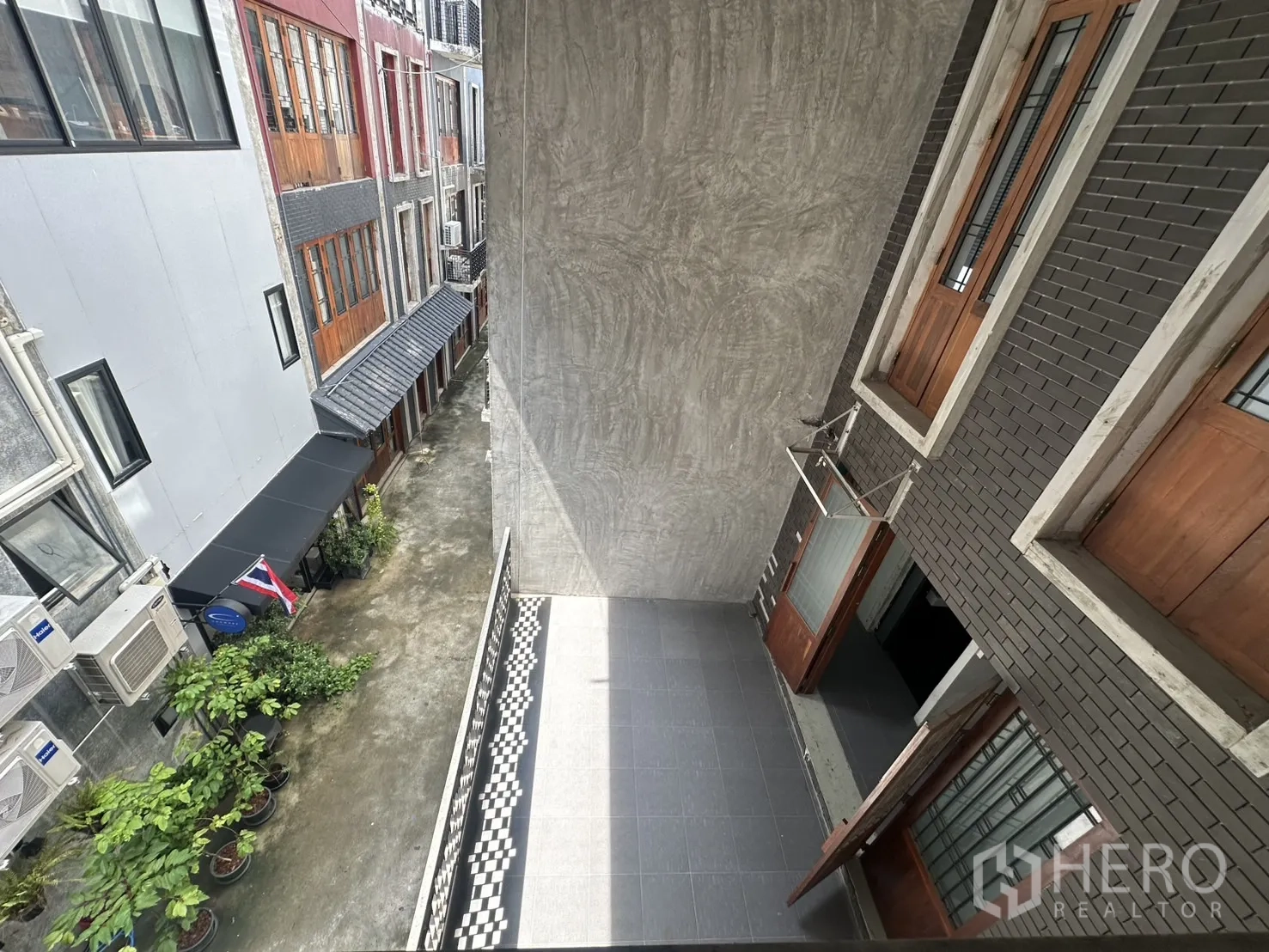 Home Office for rent in Pathum Wan, Bangkok - Top view over a narrow lane with plants, a Thai flag and adjacent balconies.