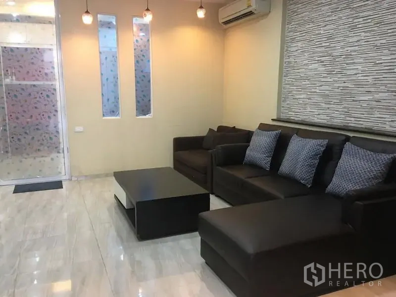 Townhouse for rent in Bang Rak, Bangkok - Cozy living room with dark leather sectional, coffee table, pendant lights, air conditioner, frosted glass door and tiled floor.