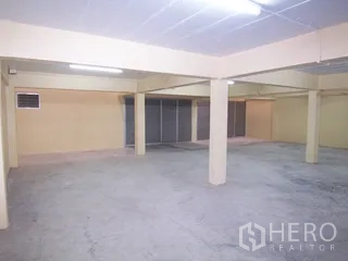 Factory for rent in Thung Khru, Bangkok - Open space with columns facing metal shutters and a small louvered window.