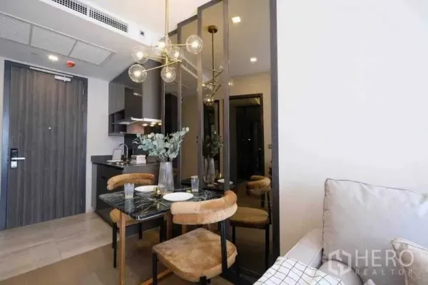 Condominium for rent in Watthana, Bangkok - Compact dining area with a marble table, pendant chandelier, mirrored panels, and a kitchenette by the entry.