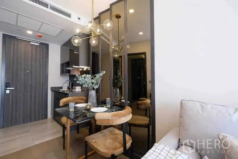 Condominium for rent in Watthana, Bangkok - Compact dining area with a marble table, pendant chandelier, mirrored panels, and a kitchenette by the entry.