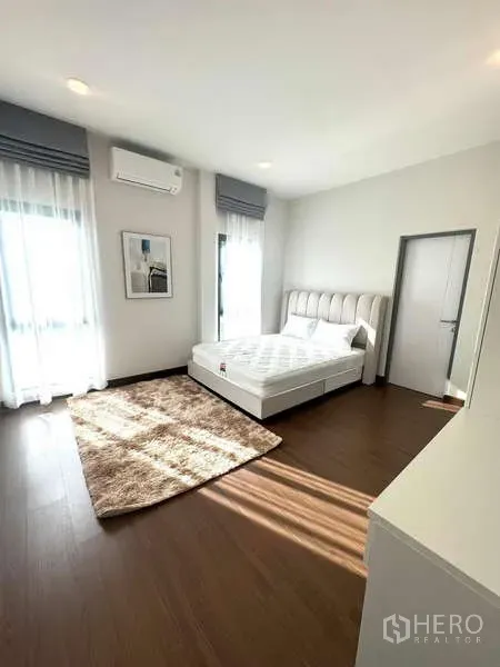 Detached House for rent in Bang Phli, Samut Prakan - Sunlit bedroom with white bed, wood flooring, soft rug and wall air conditioner