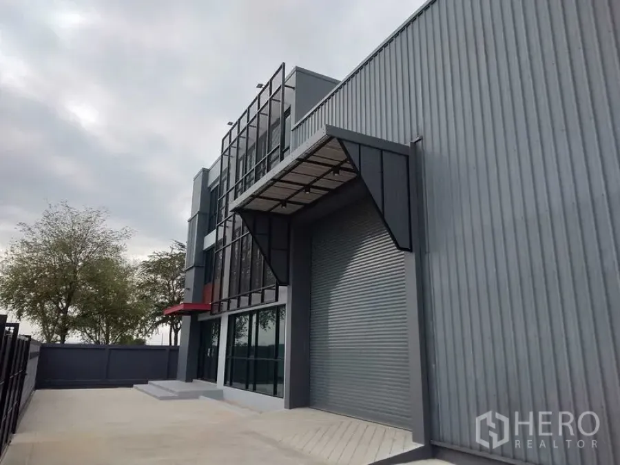 Factory for rent or sale - Warehouse loading bay featuring a large roll-up door and metal canopy beside the glass-fronted office building.