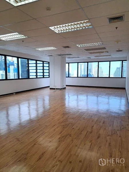 Office Space for rent in Bang Rak, Bangkok - Bright open-plan office with wood-look floors, grid ceiling lights and wraparound windows with Bangkok skyline views.