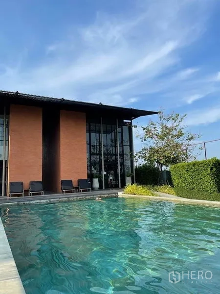 Detached House for sale in Sai Mai, Bangkok - Resort-style clubhouse with sun loungers beside an outdoor swimming pool under a blue sky.