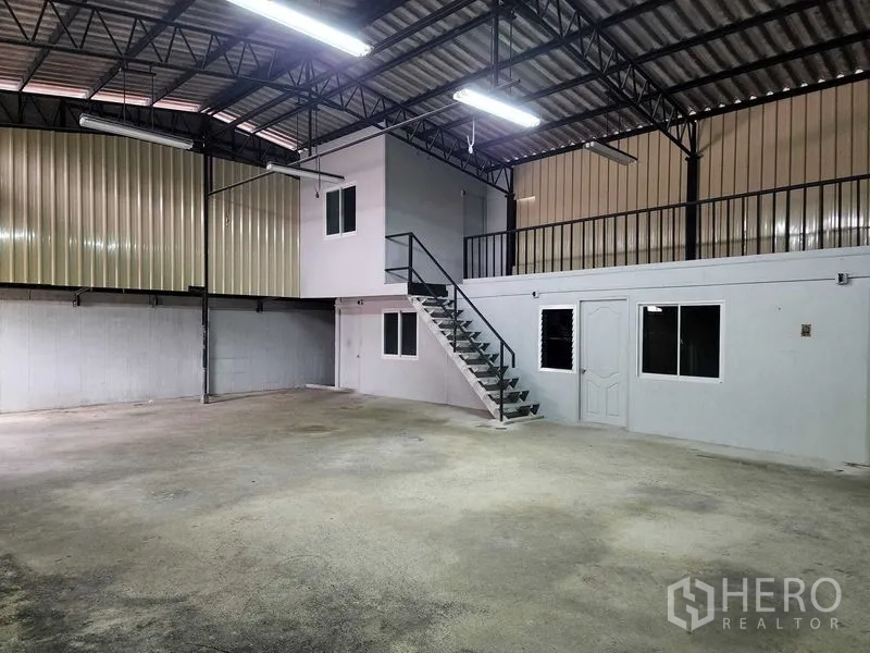 Warehouse for rent in Chatuchak, Bangkok - Warehouse floor facing the stairway to a mezzanine office with railings and windows.