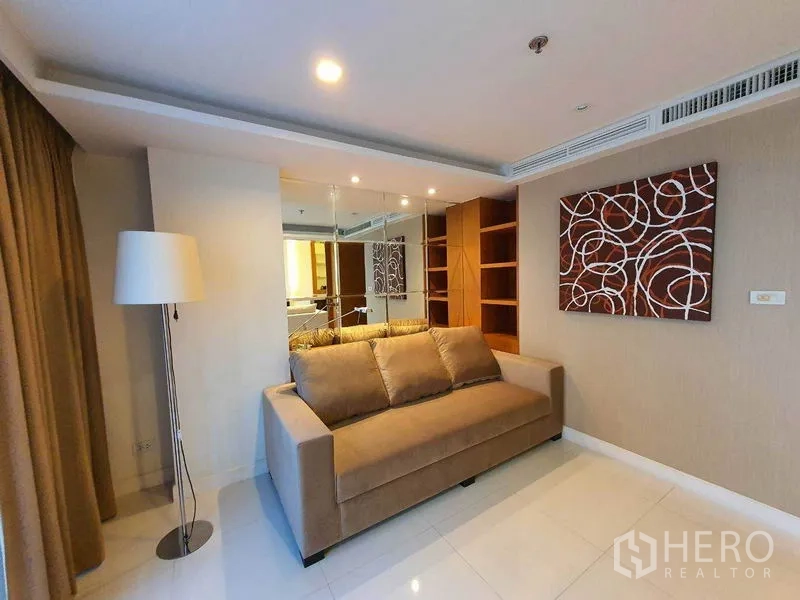 Condominium for rent in Pathum Wan, Bangkok - Cozy lounge area with sofa, mirror wall, shelving and a floor lamp.