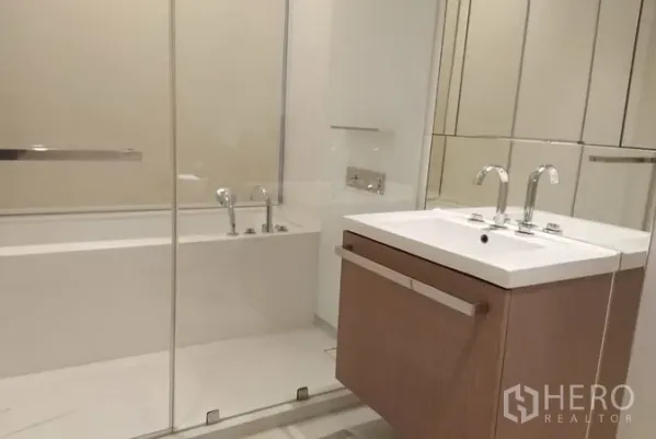 Condominium for rent in Pathum Wan, Bangkok - Contemporary bathroom featuring a glass-enclosed bathtub, floating vanity and wide wall mirrors.