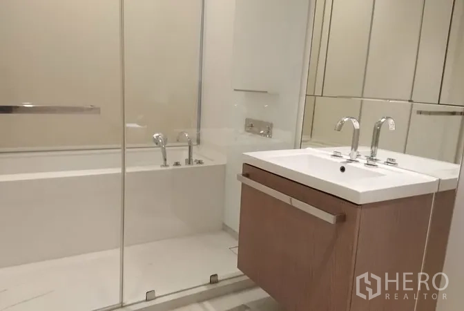 Condominium for rent in Pathum Wan, Bangkok - Contemporary bathroom featuring a glass-enclosed bathtub, floating vanity and wide wall mirrors.
