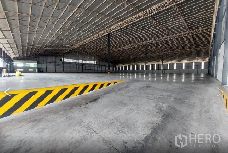 Factory for rent in Si Racha, Chon Buri - Spacious factory interior with high steel roof, ramp and striped safety barrier.