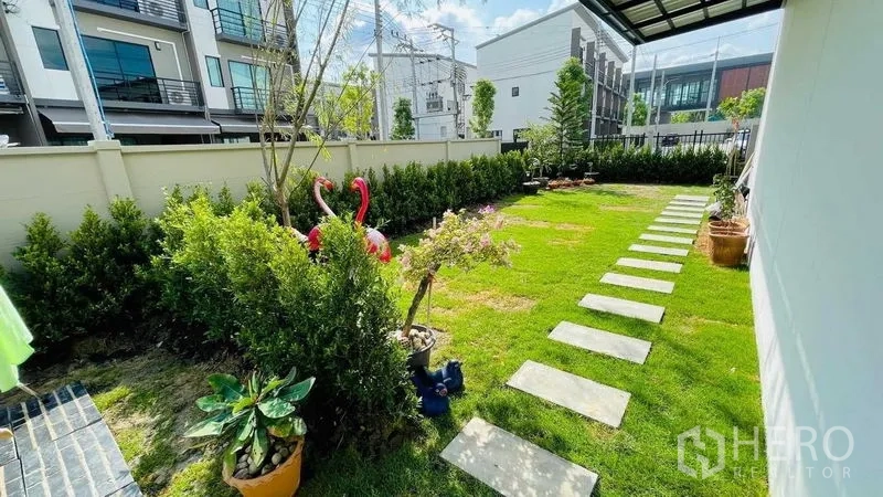 Townhouse for rent or sale in Prawet, Bangkok - Spacious private side yard with green lawn, stepping stones and potted plants.