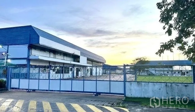 Factory for rent in Bang Bua Thong, Nonthaburi - Main gate and long factory buildings at sunset with lawn frontage.
