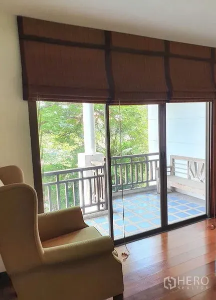 Townhouse for rent or sale in Suan Luang, Bangkok - Living area with sliding glass doors opening to a blue-tiled balcony and leafy views.
