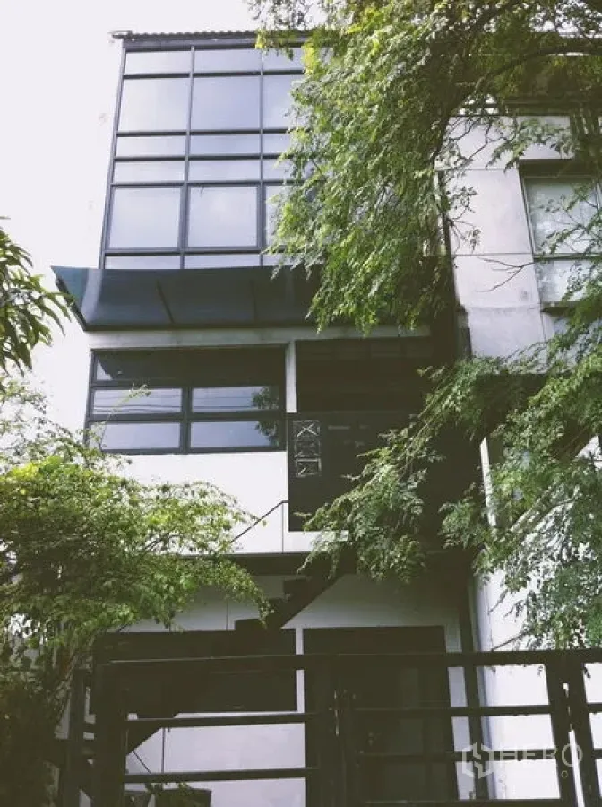 Home Office for rent in Chatuchak, Bangkok - Tree-shaded front facade with large windows and a metal gate.