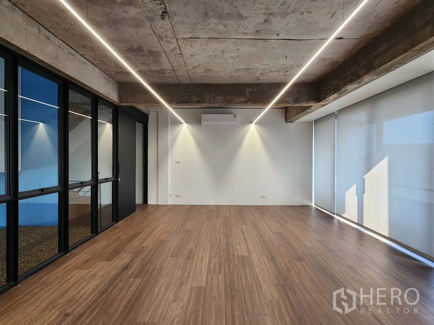 Home Office for rent in Chatuchak, Bangkok - Open-plan office with wood floors, exposed concrete ceiling, LED strip lights, and glass partition.