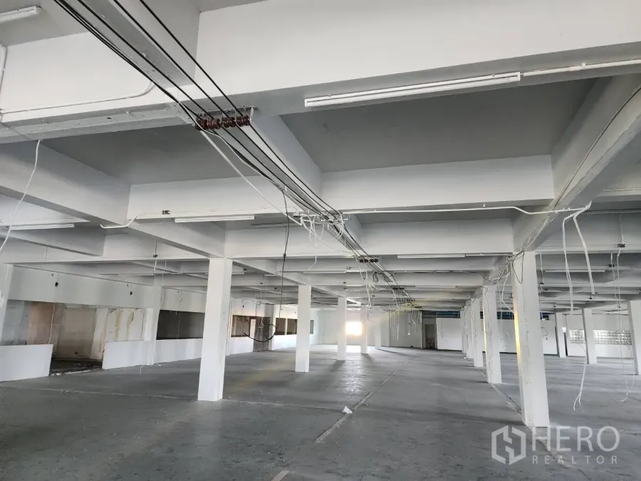 Factory for rent or sale in Khlong Toei, Bangkok - Open-plan factory floor with white concrete columns, exposed wiring and fluorescent lighting.