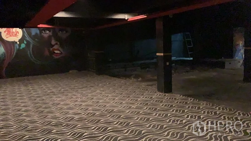 Shophouse for rent in Watthana, Bangkok - Spacious dark interior with wave-pattern carpet, black columns, and a large graffiti mural on the wall.