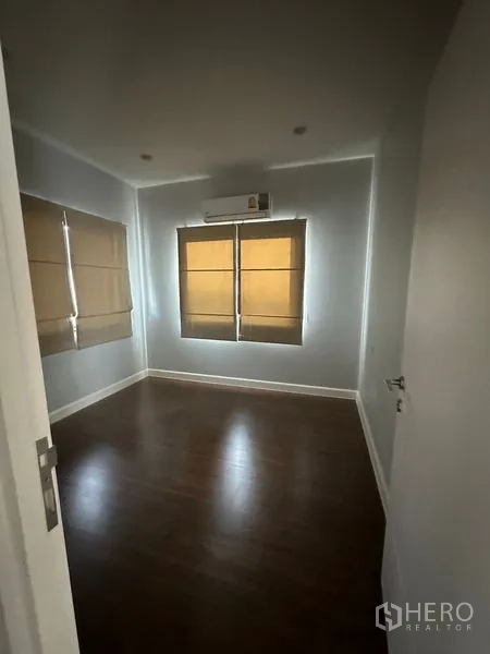 Detached House for rent or sale in Lam Luk Ka, Pathum Thani - Second bedroom with air conditioning, two windows and wood-style flooring.