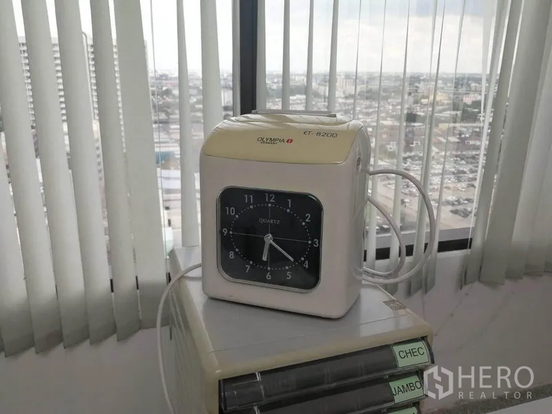 Office Space for rent in Bang Na, Bangkok - Time clock beside a window with vertical blinds and a panoramic city view.