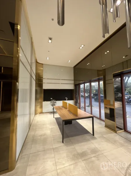 Shophouse for rent in Phra Khanong, Bangkok - Ground‑floor retail space with large street‑facing windows, tiled floor and long worktable under spotlights.