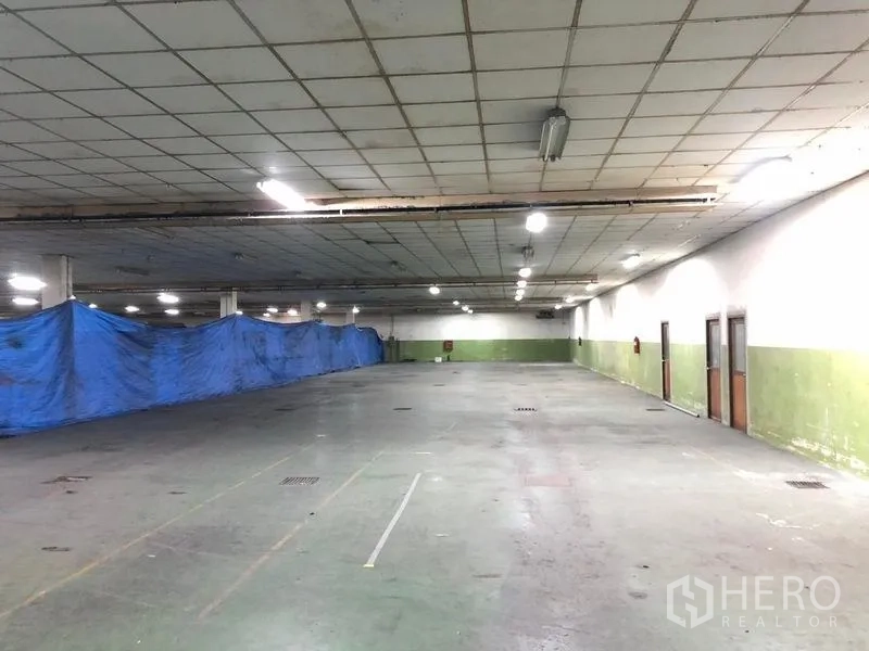 Factory for rent in Lat Krabang, Bangkok - Open factory floor with a blue tarpaulin divider, floor drains and multiple side doors.