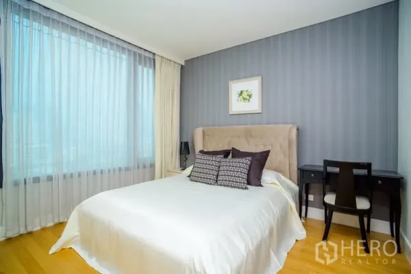 Condominium for rent in Khlong Toei, Bangkok - Third bedroom with upholstered headboard, desk, city views through large windows and a blue feature wall.