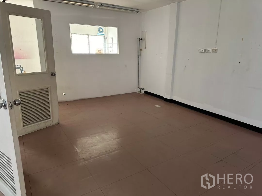 Shophouse for sale in Watthana, Bangkok - Simple white room with pink tiles and a door with glass panel.