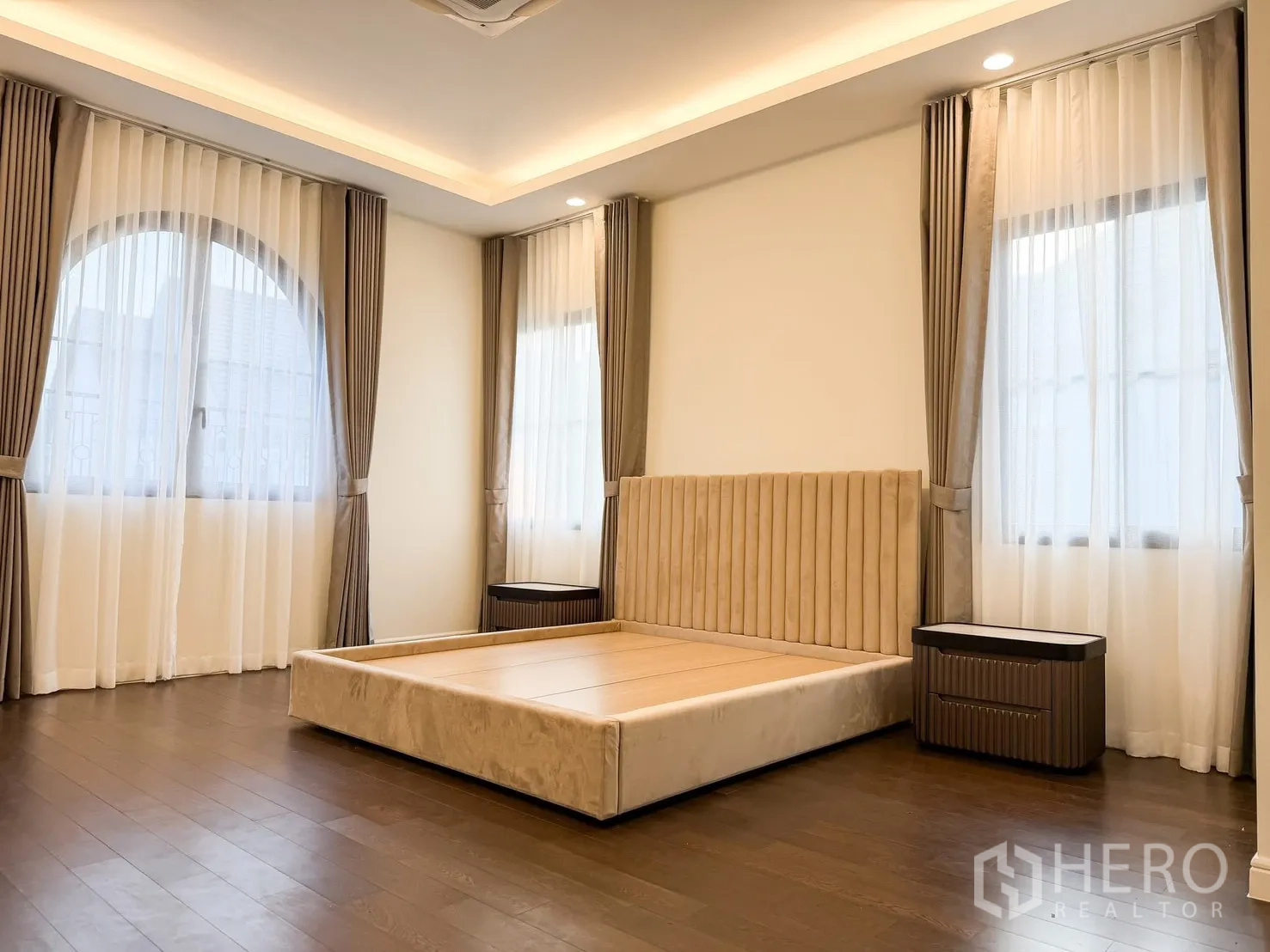 Detached House for rent in Bang Khen, Bangkok - Spacious bedroom with beige upholstered bedframe, cove ceiling lights and multiple windows.