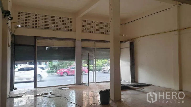 Shophouse for rent in Phra Khanong, Bangkok - Ground-floor retail space with glass storefront and roller shutters opening to the street.