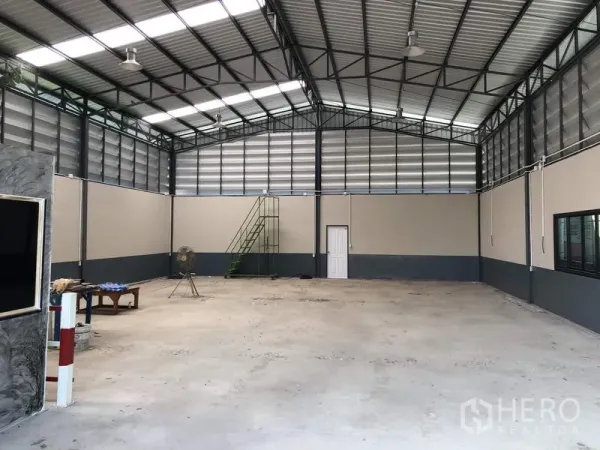 คลังสินค้า ขายในPathum Thani - ภาพกว้างภายในโกดัง มีแผงระบายอากาศ โคมไฟแขวน หน้าต่าง และบันไดเหล็กสีเขียว