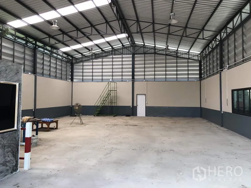 คลังสินค้า ขายในPathum Thani - ภาพกว้างภายในโกดัง มีแผงระบายอากาศ โคมไฟแขวน หน้าต่าง และบันไดเหล็กสีเขียว