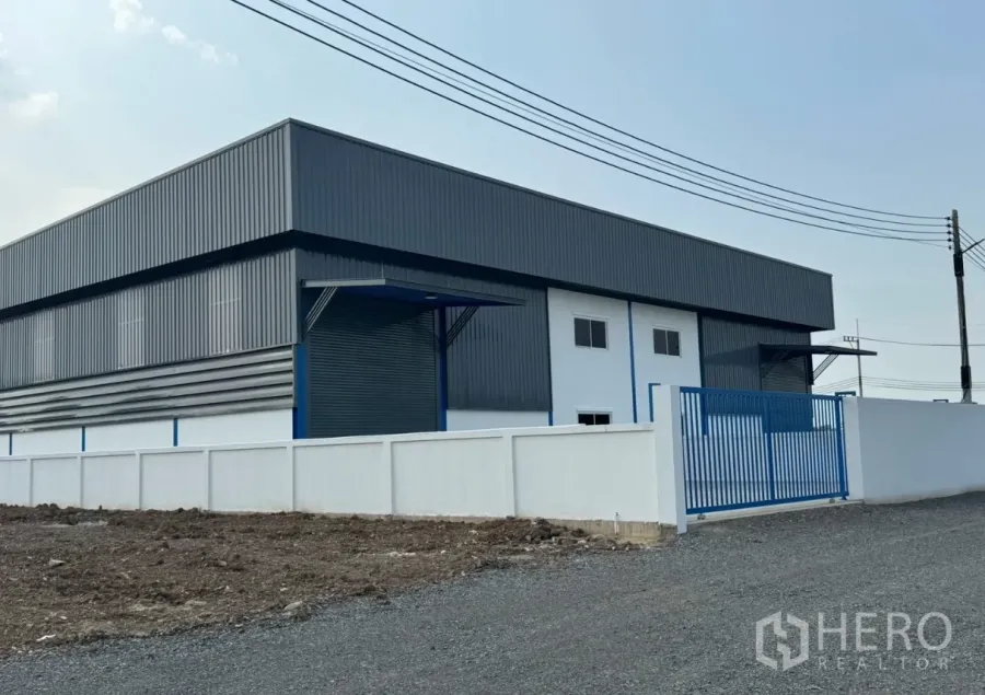 Warehouse for rent in Khlong Luang, Pathum Thani - Exterior view of metal-clad warehouse with perimeter wall and gated entrance.