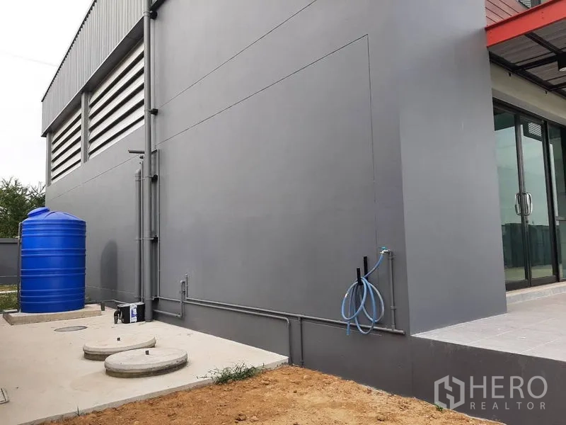 Factory for rent or sale in Lam Luk Ka, Pathum Thani - Exterior utility zone with blue water tank, piping and service access.